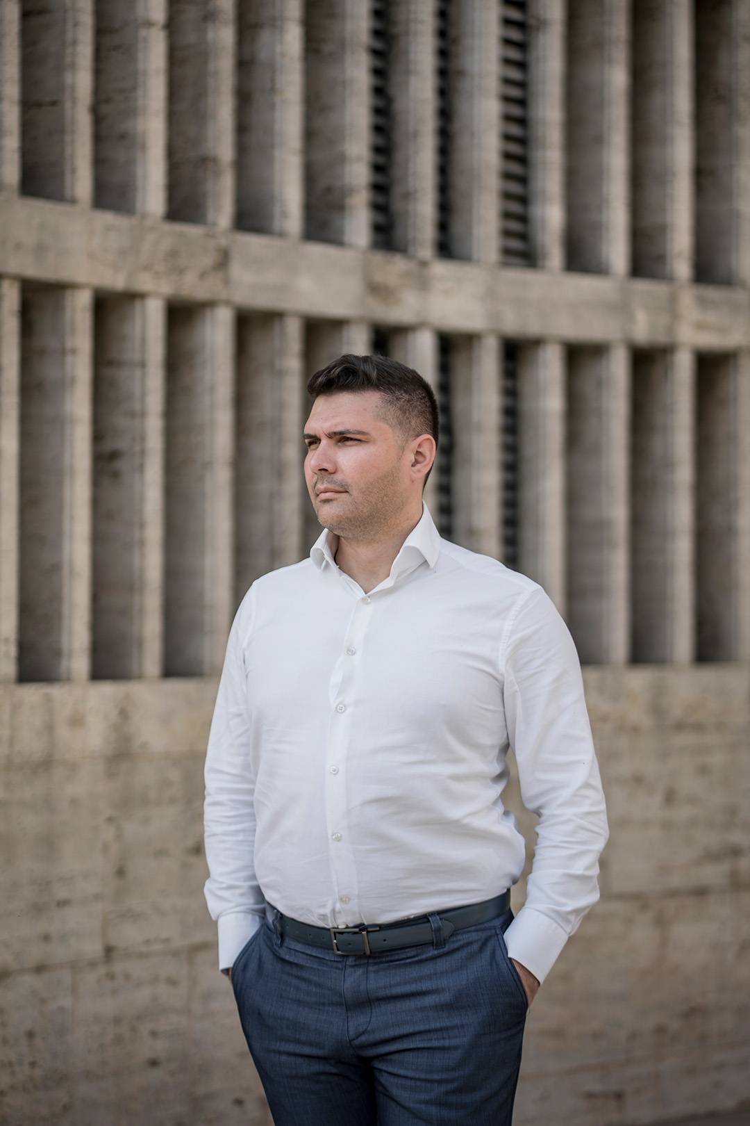 Lucian Mustata stands against a post-Communist architectural concrete building.