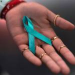 An open hand holds a turquoise memorial ribbon loop