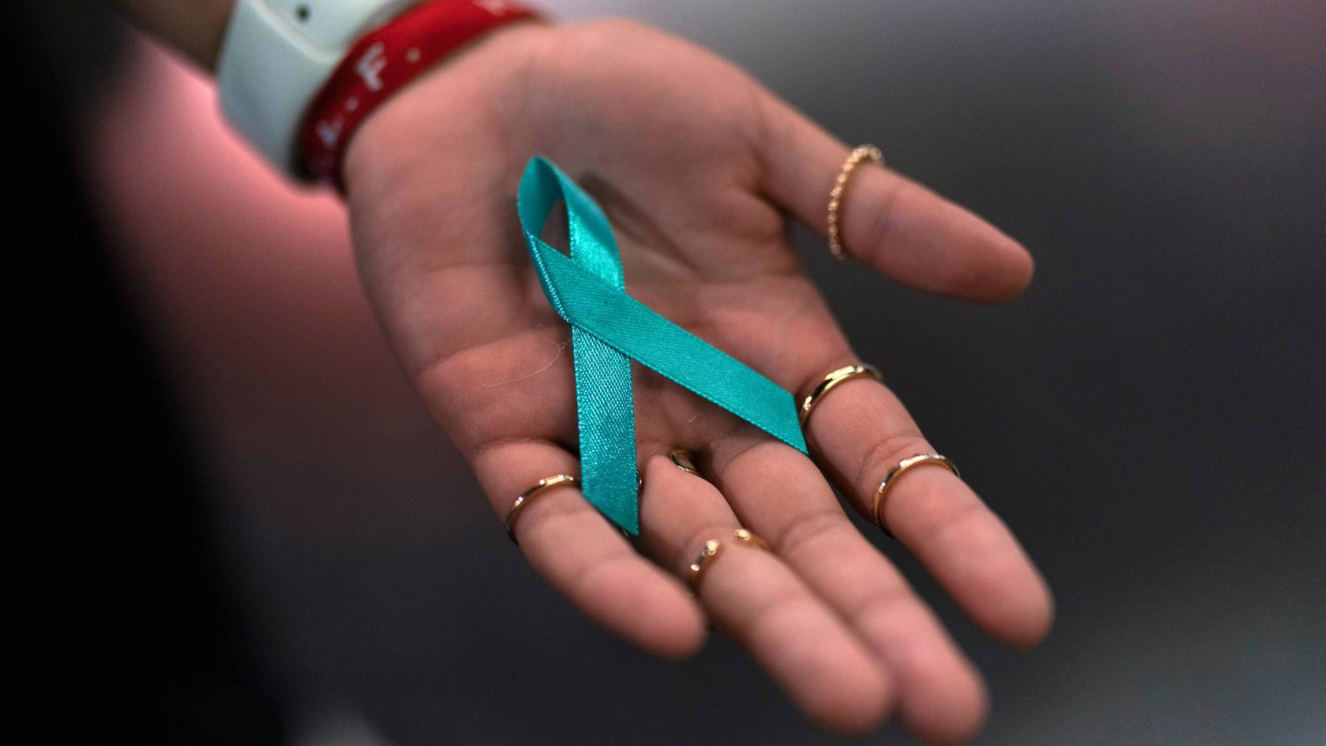 An open hand holds a turquoise memorial ribbon loop