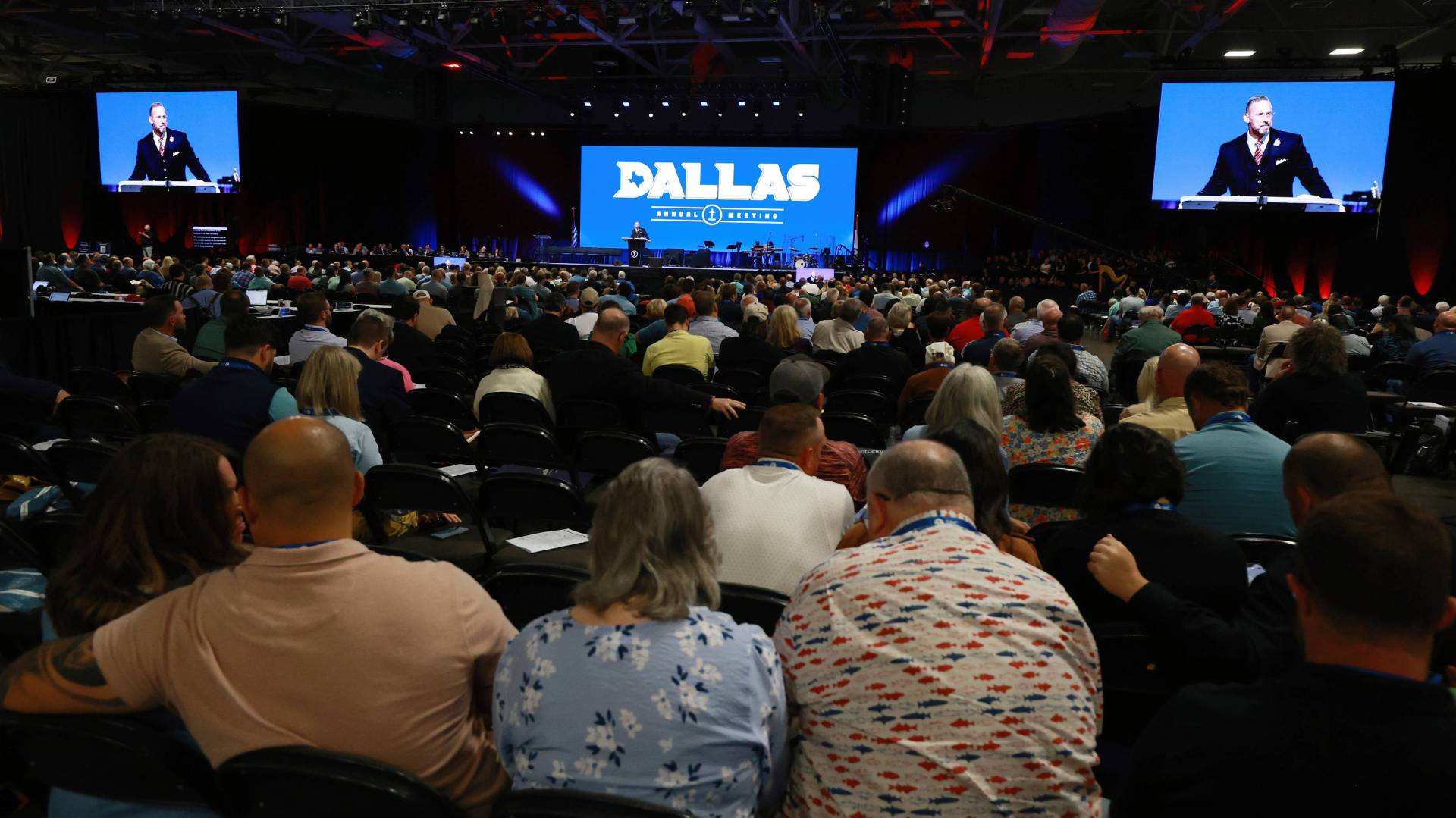 Crowd in convention center with three screens.