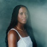 Headshot of Adira Polite on blue background with light obscuring her face