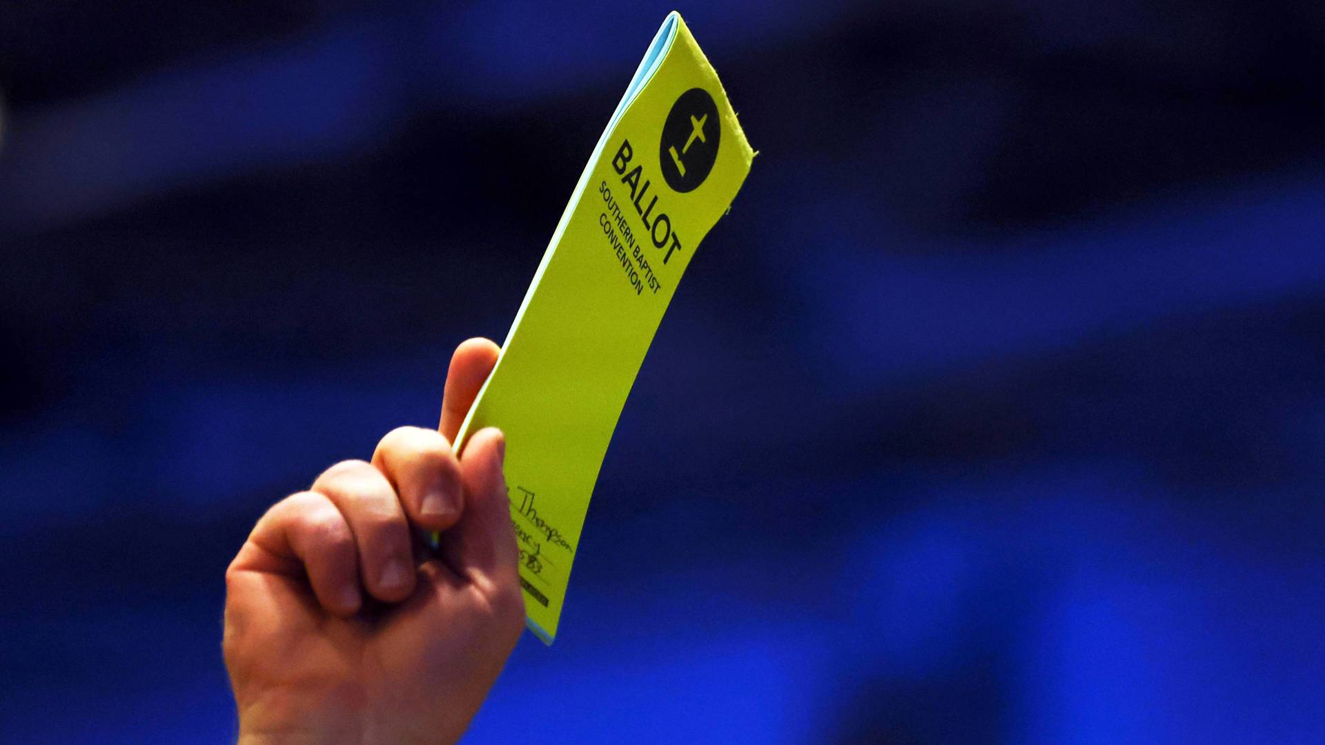 A yellow paper ballot held in the air with a hand