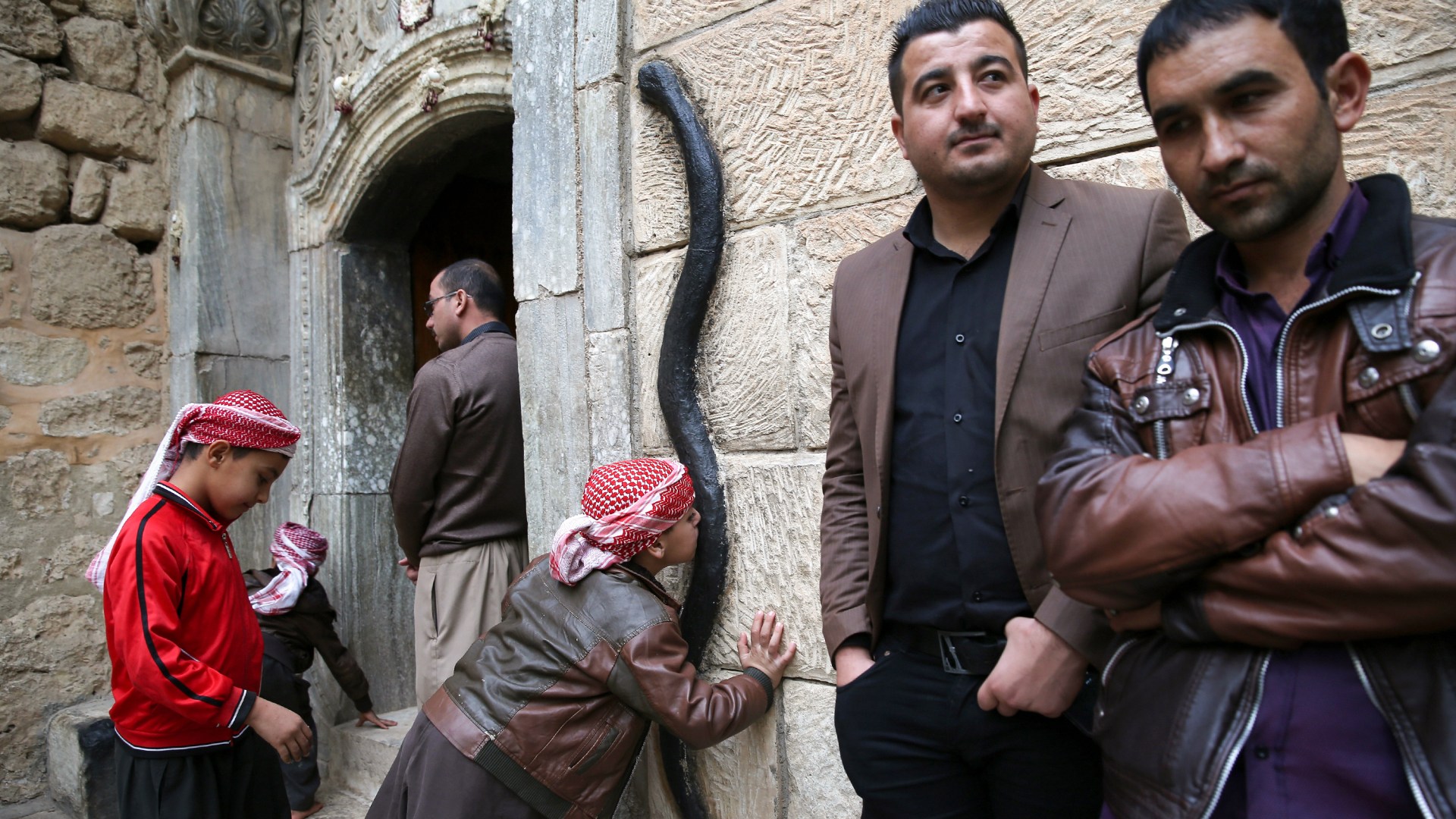 A Yazidi boy kisses a figure of a black snake at the entrance of the Temple of Lalish in Iraq.