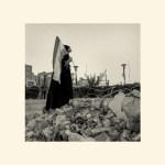A woman standing in rubble with an Iranian flag.