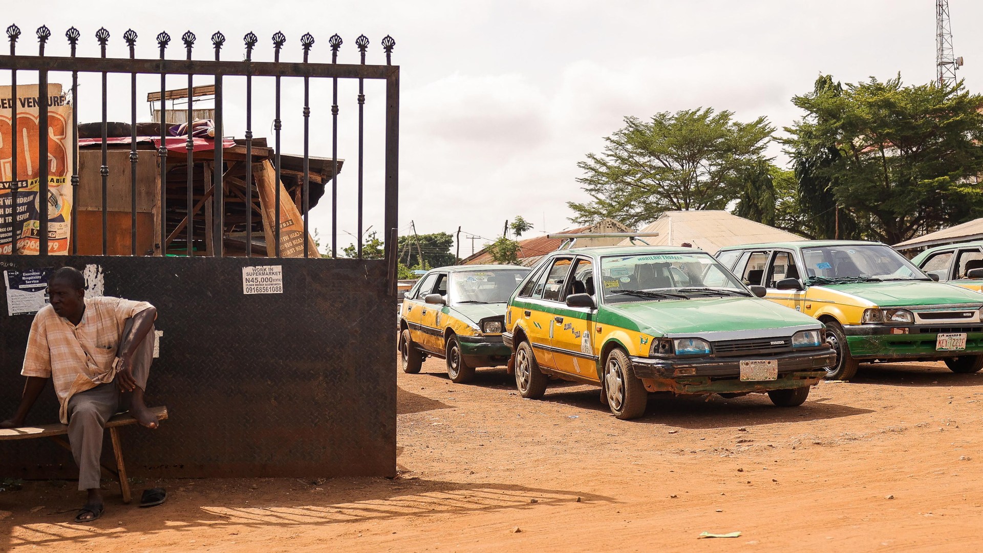 Local taxis are seen parked in a lot as a man sits by its entrance in Nigeria