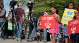 Child holds sign saying "Let Kids be Kids" and another "Bring Back the Opt-Out"