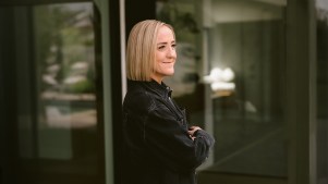 Photograph of Christine Caine standing in a black jacket with arms crossed outside of a modern house.