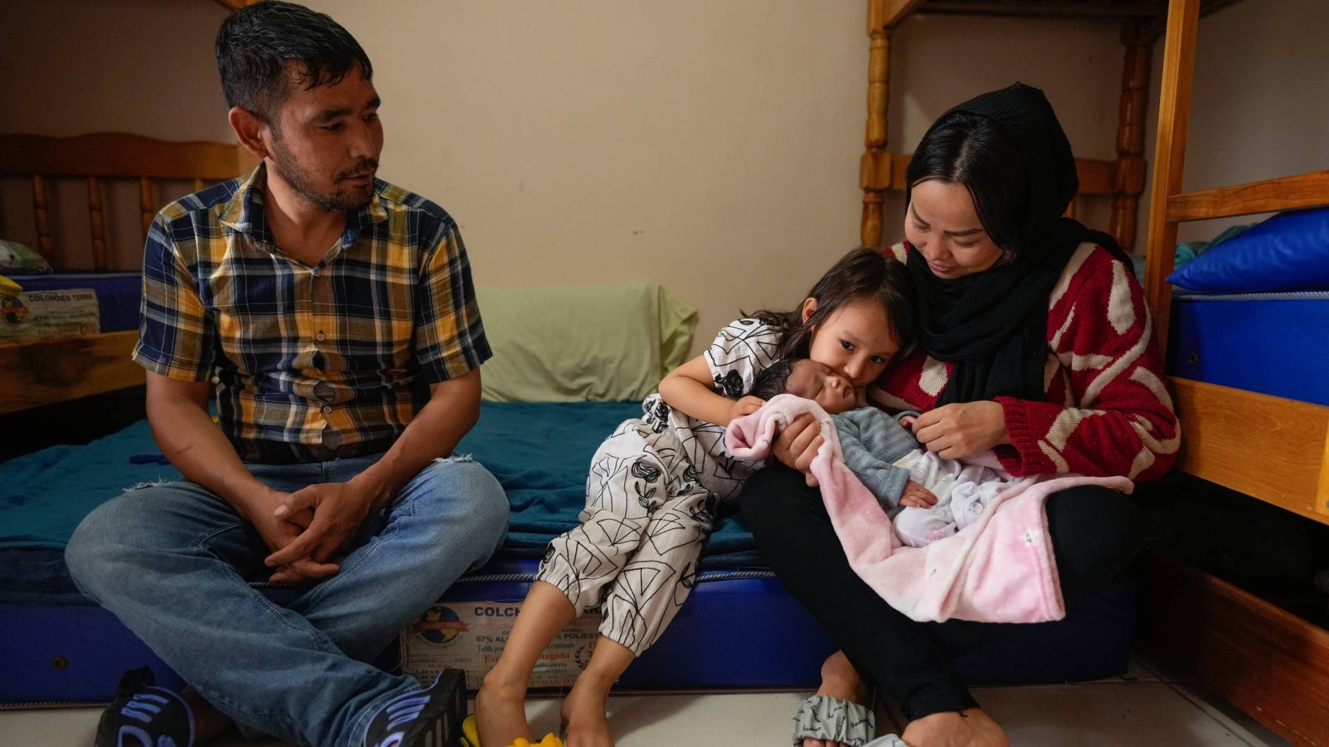 A father, mother, daughter, and baby sitting on bunk beds in a shelter in Praia Grande, Brazil.