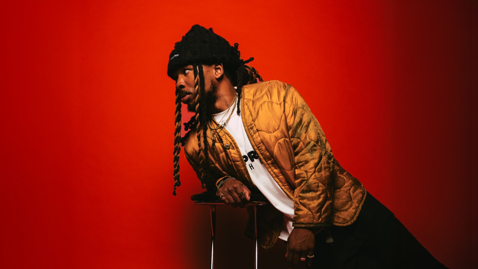 nobigdyl. leaning on a stool in front of a red background