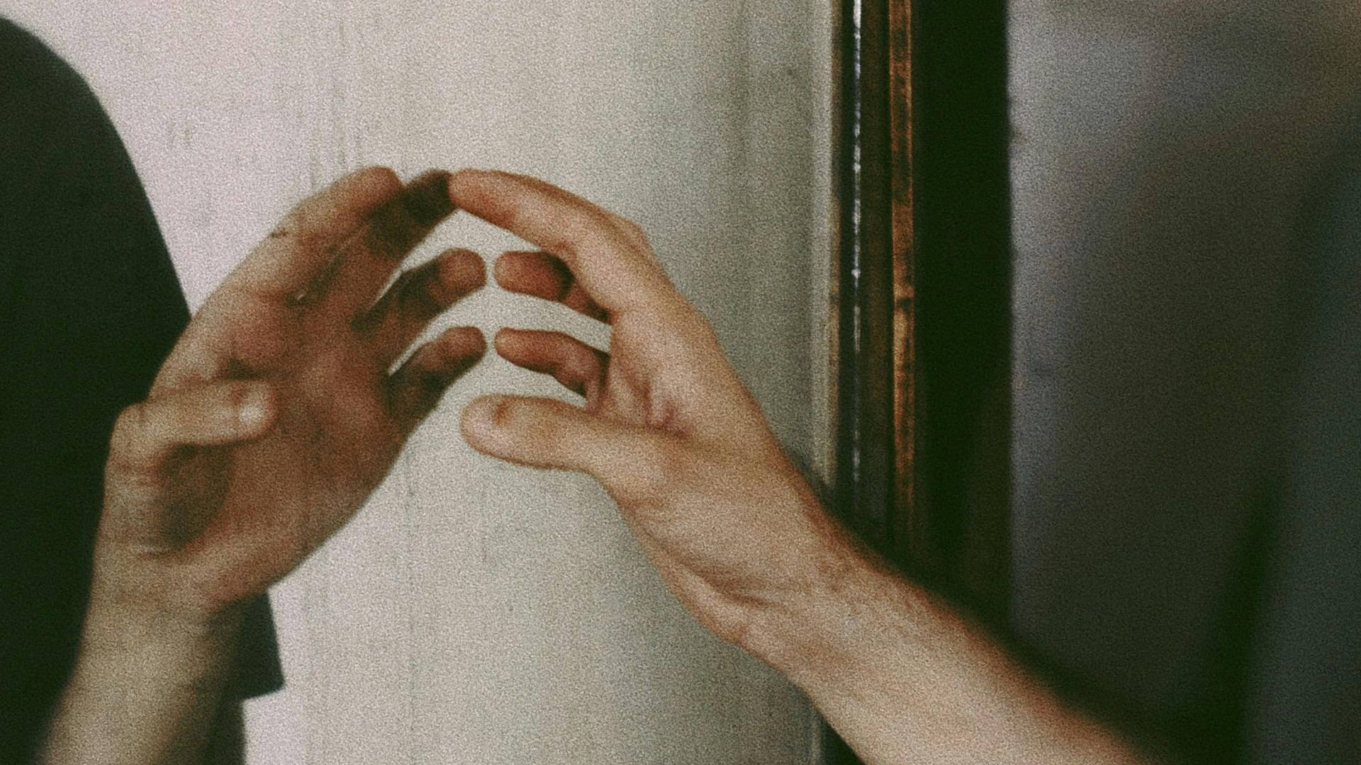A hand reaching towards its reflection in the mirror