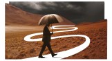 A man walking with an umbrella in the wilderness into a storm.
