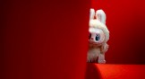 Labubu toy looking out behind a couch