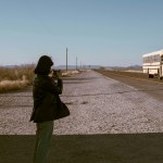 A girl standing in a desert as a bus drives by in Texas.