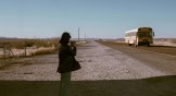 A girl standing in a desert as a bus drives by in Texas.