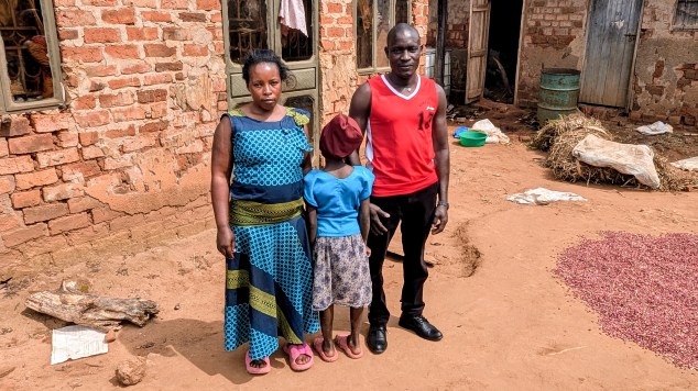 N.K., age 9, stands between her parents Namatovu Joyce and Sserwanja Dick.