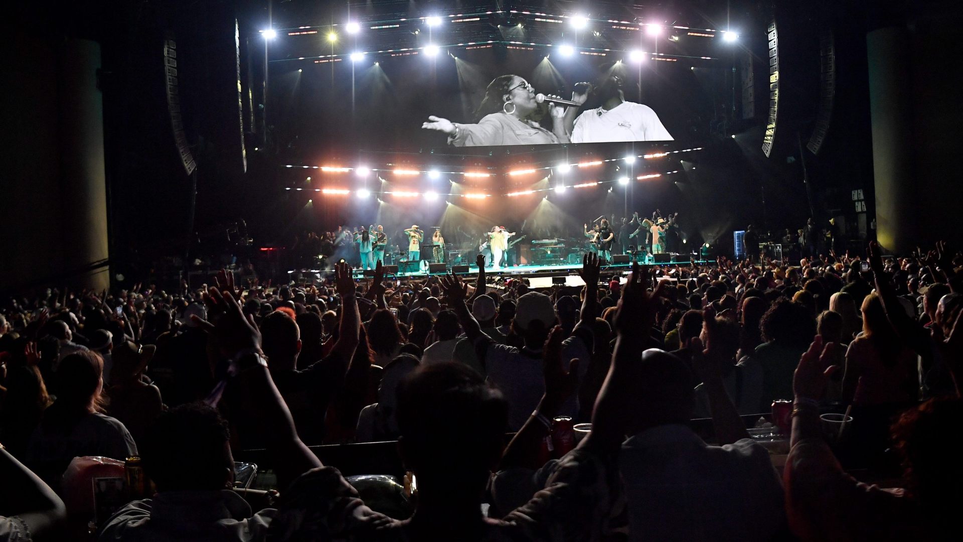 Stage with lights and a crowd with hands raised. Naomi Raine pictured on screen.
