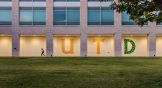 A student walks outside a building with the UTD logo in green and yellow at twilight.