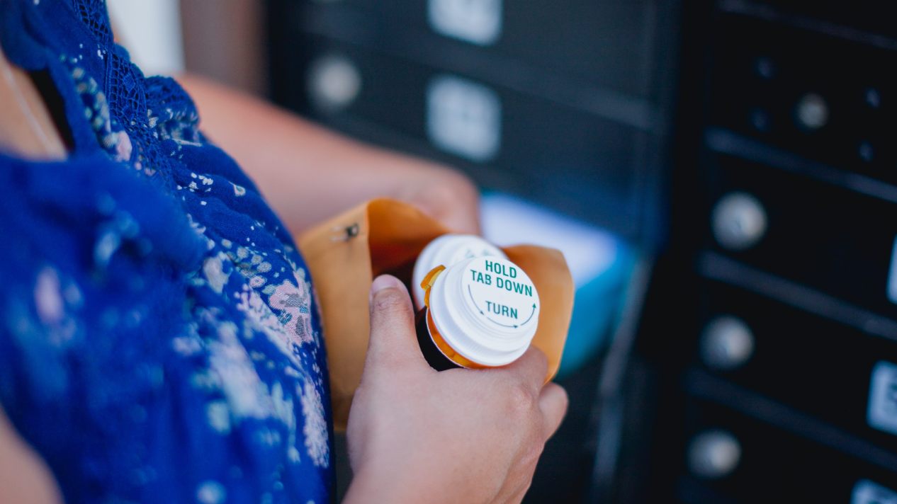 A woman holds a pill bottle in a manila envelope in a mail room.