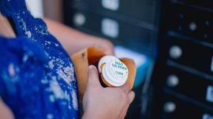 A woman holds a pill bottle in a manila envelope in a mail room.
