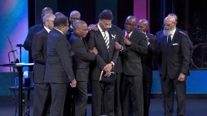Men in suits surround Tony Evans to pray for him.