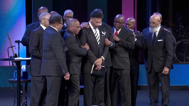 Men in suits surround Tony Evans to pray for him.