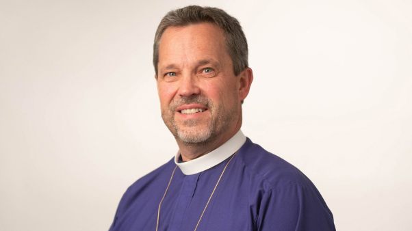 Steve Wood in white clerical collar and purple shirt with gold necklace.