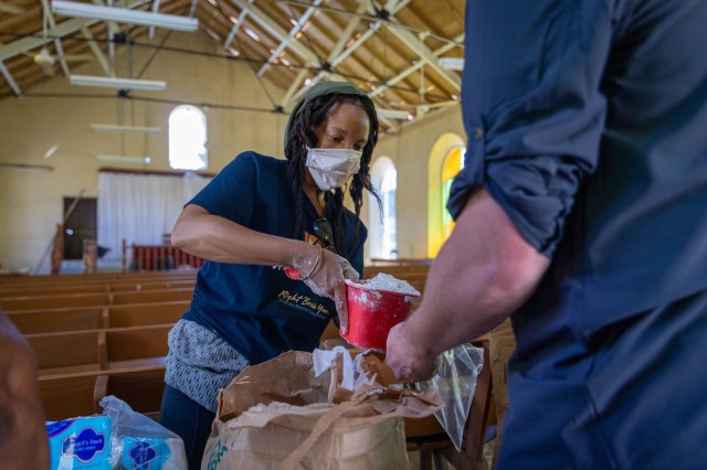 A woman in a mask stands in a church sanctuary scooping flour into a bag.