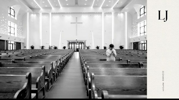 Black and white photo of a church with many empty pews and only one person standing and praying