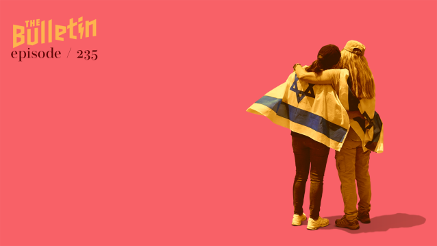 Two women facing away, one has an Israel flag draped over her shoulders, the other woman has her arm around the first.