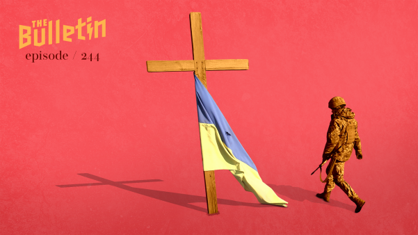 Soldier walking past a cross draped with a Ukrainian flag.