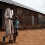 A disabled man walking with a cane and help from his child.
