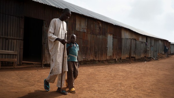 A disabled man walking with a cane and help from his child.
