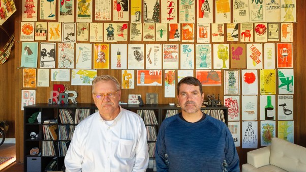 Lance Kagey (L) and Tom Llewellyn (R) standing in front of a wall displaying their hand-printed posters.