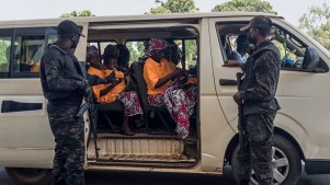Security officers stand guard next to a bus carrying freed worshippers at the Government House in Kaduna.