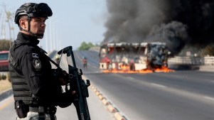 A member of the Prosecutor's Office stands guard near a burning bus after it was set on fire by organized crime groups in response to an operation to arrest a high-priority security target in Mexico.