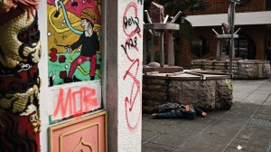 Person lying on a sidewalk in a graffiti-covered Chinatown street.