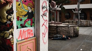 Person lying on a sidewalk in a graffiti-covered Chinatown street.