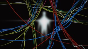 Blurred glowing human figure behind a tangle of colorful cables against a dark background.