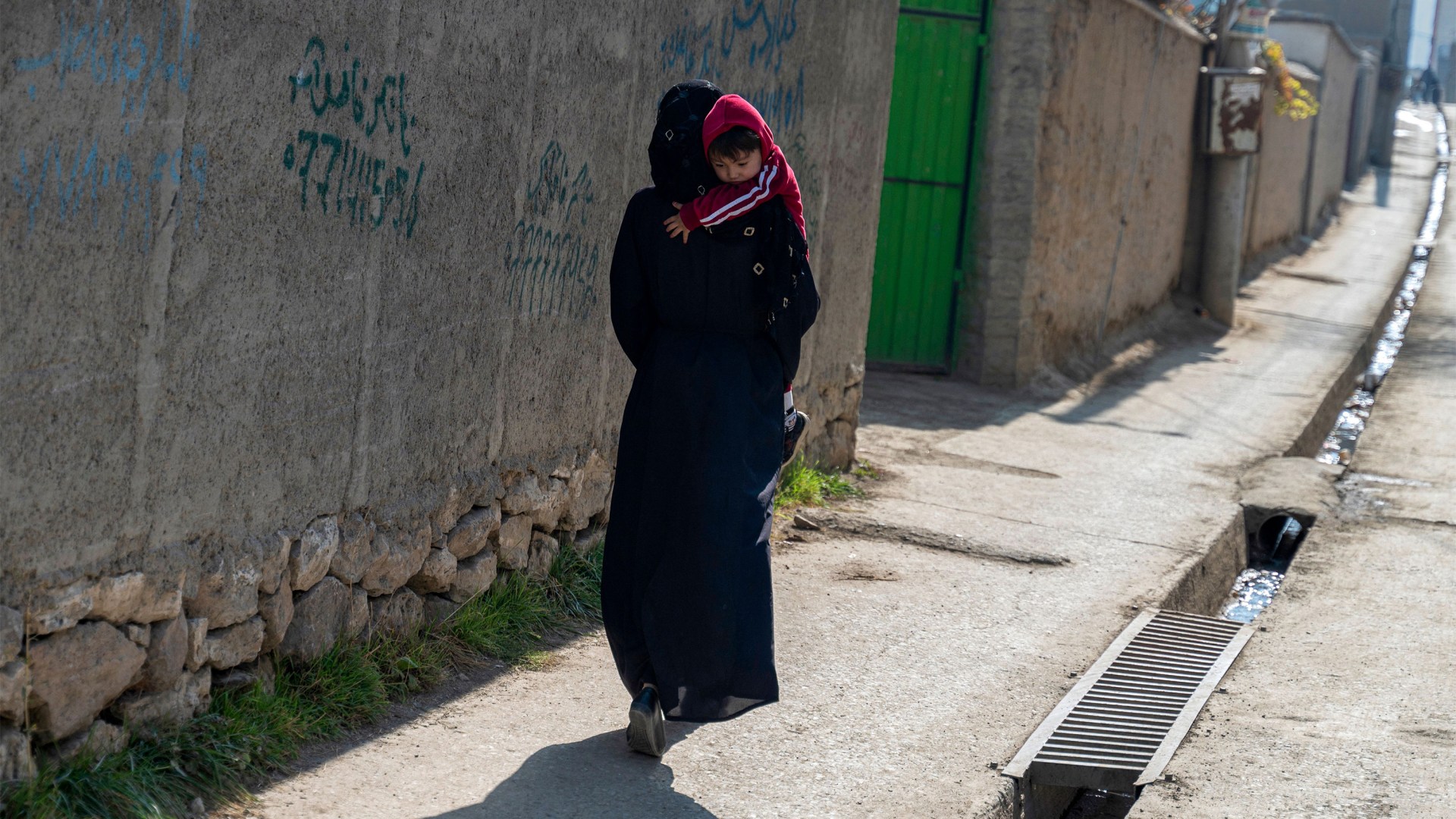An Afghan Hazara woman carrying her child along a street in Dasht-e-Barchi in Kabul.