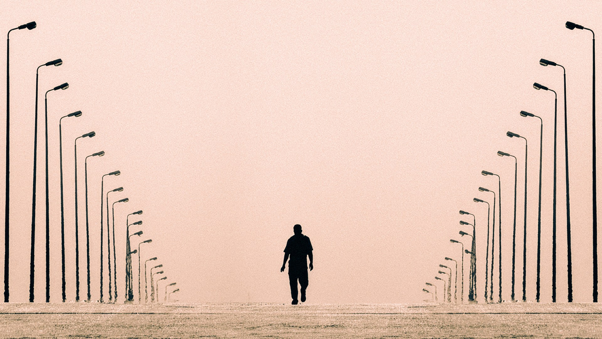 A lone silhouetted figure walks down an empty corridor flanked by two converging rows of tall streetlights against a hazy pink sky.