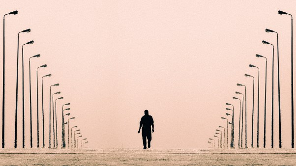 A lone silhouetted figure walks down an empty corridor flanked by two converging rows of tall streetlights against a hazy pink sky.